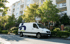 Weißer Mercedes-Benz Transporter mit blau-grünem Logo parkt auf einer Straße vor einem Apartmentgebäude.