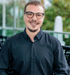Ein lächelnder Mann mit Brille und schwarzem Hemd blickt geradeaus.
