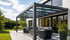 Modernes, freistehendes Carport mit transparentem Dach und grauem Metallrahmen auf gepflasterter Einfahrt.