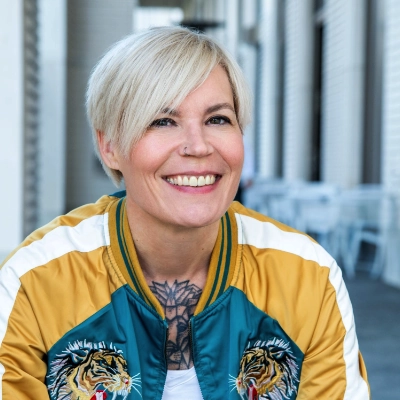 Frau blonde kurze Haare bunte Jacke Tattoo