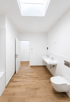 Modernes weißes Badezimmer mit Oberlicht, Holzoptik-Fliesen, Doppelwaschbecken und wandhängendem WC.