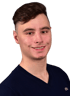 Ein junger Mann mit kurzen braunen Haaren und einem dunkelblauen V-Pullover lächelt in die Kamera.