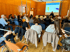 Referent präsentiert vor Publikum in einem Konferenzraum mit Holzverkleidung, auf der Leinwand eine Grafik.