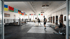 Mehrere Boxer trainieren in einem Fitnessstudio mit Boxring, Sandsäcken und Nationalflaggen an der Wand.