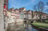 Historische Fachwerkhäuser entlang eines Flusses mit einer Steinbrücke unter blauem Himmel.