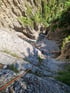 Zwei Personen seilen sich in einer felsigen Schlucht mit Fluss und Bäumen ab.