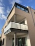 Modernes Gebäude mit hellem Putz, Balkon mit Glasgeländer und verglaster Dachterrasse unter blauem Himmel.