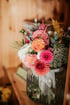 Bunter Blumenstrauß mit Dahlien in Rosa, Orange und Rot in einer geriffelten Glasvase mit weißer Schleife auf Holzregal.