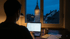 Ein Gründer sitzt spät nachts im Schein einer Schreibtischlampe vor seinem Laptop und bearbeitet Formulare für die Buchhaltung. Ein Blick durch das Fenster auf einen beleuchteten Uhrturm in der Dunkelheit unterstreicht die späte Stunde.