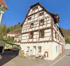 Ein mehrstöckiges historisches Fachwerkhaus mit weißer Fassade, dunklen Holzbalken und einem kleinen Laden im Erdgeschoss.