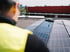 Eine Person in gelber Weste beobachtet die Reinigung von Solarmodulen auf einem Dach.