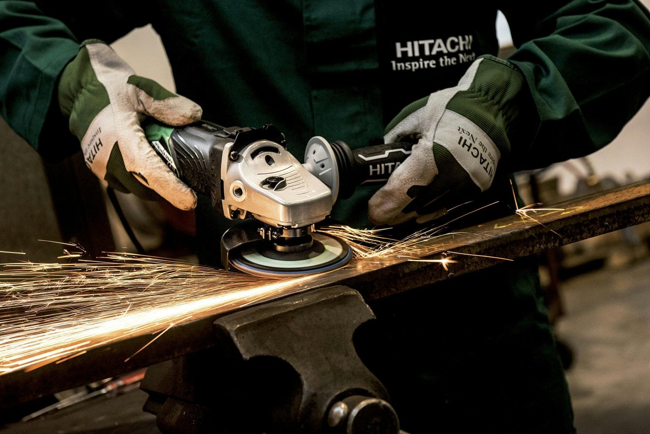 Ein Handwerker bearbeitet Metall mit einem Hitachi Winkelschleifer, wobei Funken fliegen.