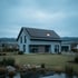 Modernes Einfamilienhaus mit Photovoltaikanlage auf dem Satteldach, Rasenfläche und kleinem Teich in der Abenddämmerung.
