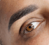 Nahaufnahme eines braunen Auges mit einer präzise geformten, dunkelbraunen Augenbraue nach einer Microblading-Behandlung.