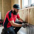 Handwerker auf Gerüst montiert Fassadenverkleidung mit Akkuschrauber neben großen Fenstern.