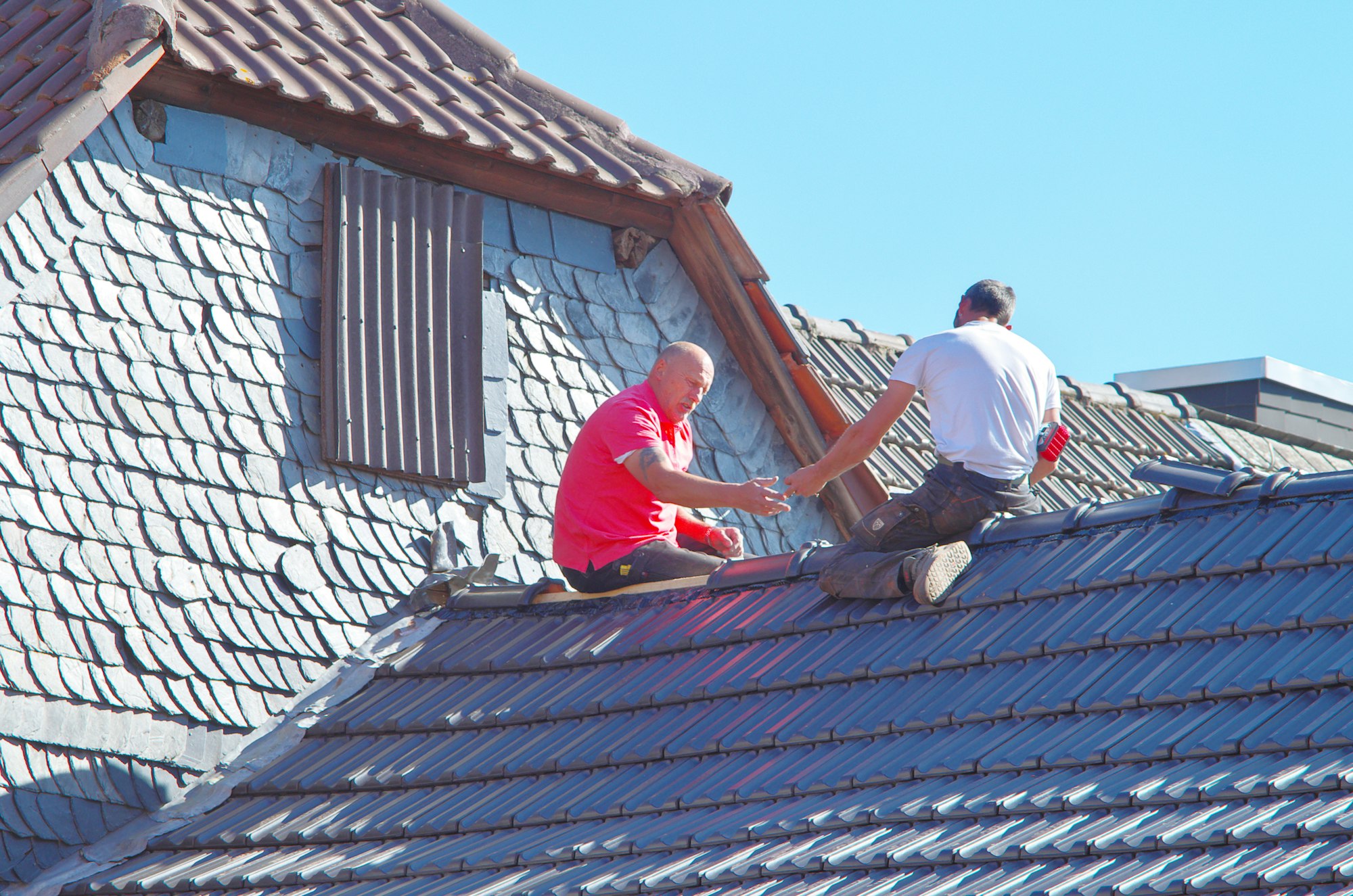 Two roofers fitting shingles on a house roof, the cold weather installation work that needs hand-sealing on a Joshua, TX winter job.