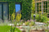 Modernes Gebäude mit vertikaler Fassadenbegrünung, Holzspalier und einem Gartenbeet mit gelben und violetten Wildblumen.