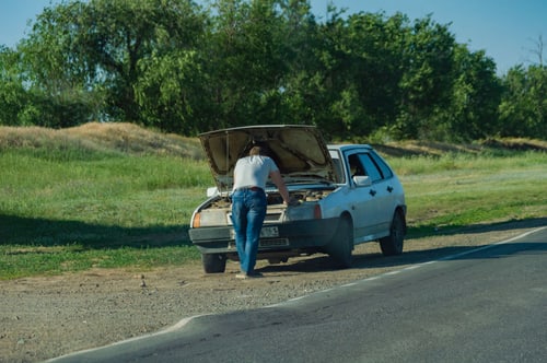 Car stopped on a freeway shoulder with its hood raised after overheating in Corona, CA