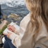 Frau mit blondem Haar schreibt in ein Notizbuch, im Hintergrund ist Wasser zu sehen.