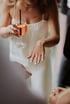A person in a white dress holds an Aperol Spritz while displaying a ring on their left hand with light blue nail polish.