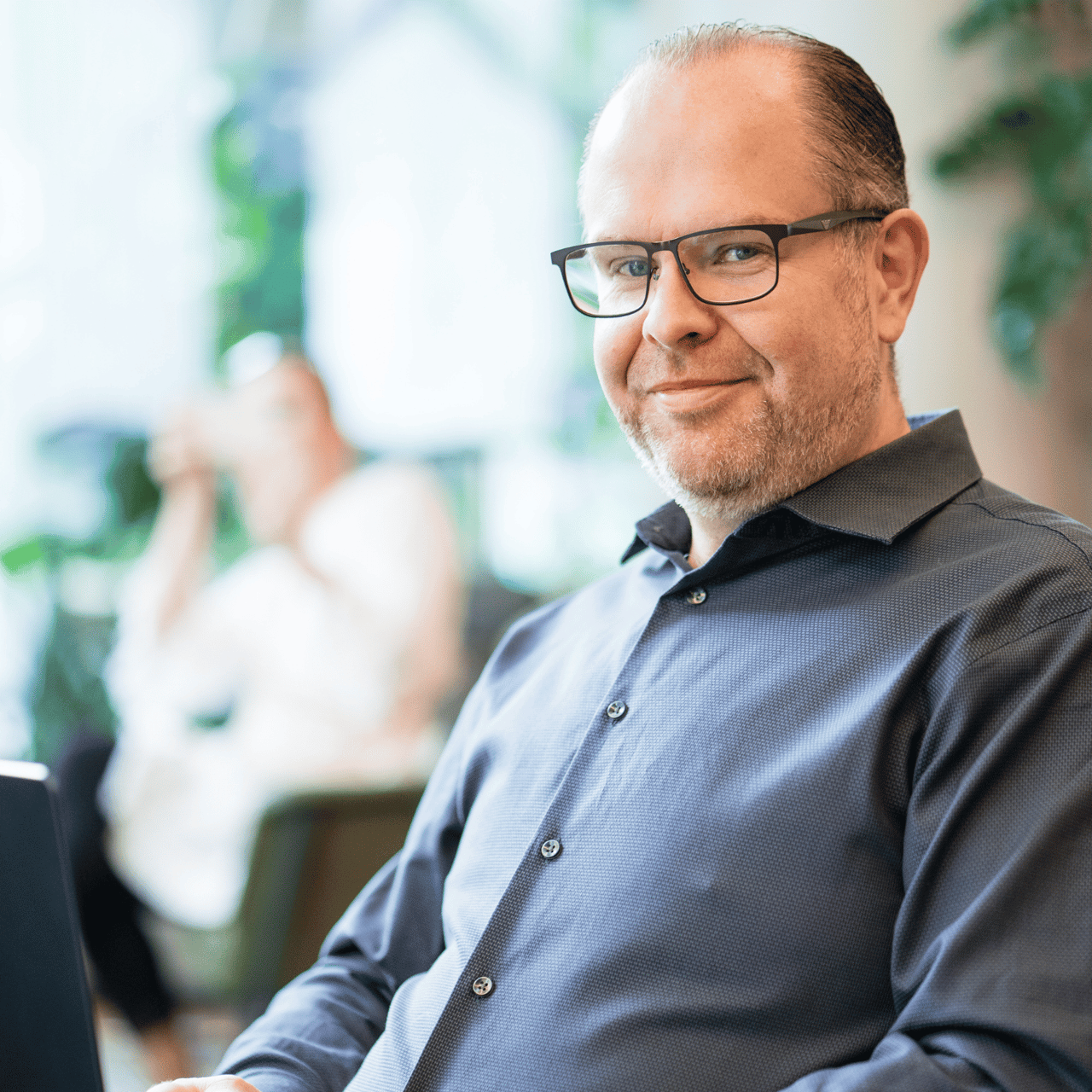 Lächelnder Mann mit Brille und grauem Hemd blickt in die Kamera.