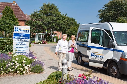 Zwei Frauen stehen neben einem Kleinbus mit Diakonie-Beschriftung.