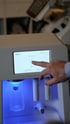 Ein Finger bedient das Touch-Display des deep2 Kosmetikgeräts mit blau leuchtender Chromotherapie-Station.