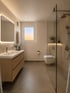 Modernes Badezimmer mit Holz-Waschtisch, beleuchtetem Spiegel, wandhängendem WC und ebenerdiger Glasdusche.