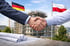 Händedruck vor Baustelle mit deutscher und polnischer Flagge, Baupläne liegen im Vordergrund.