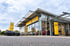 Außenansicht eines modernen Opel Autohauses mit Glasfront, gelben Markenschildern und geparkten PKW unter bewölktem Himmel.