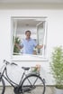 Mann öffnet ein Fenster mit Insektenschutz-Spannrahmen