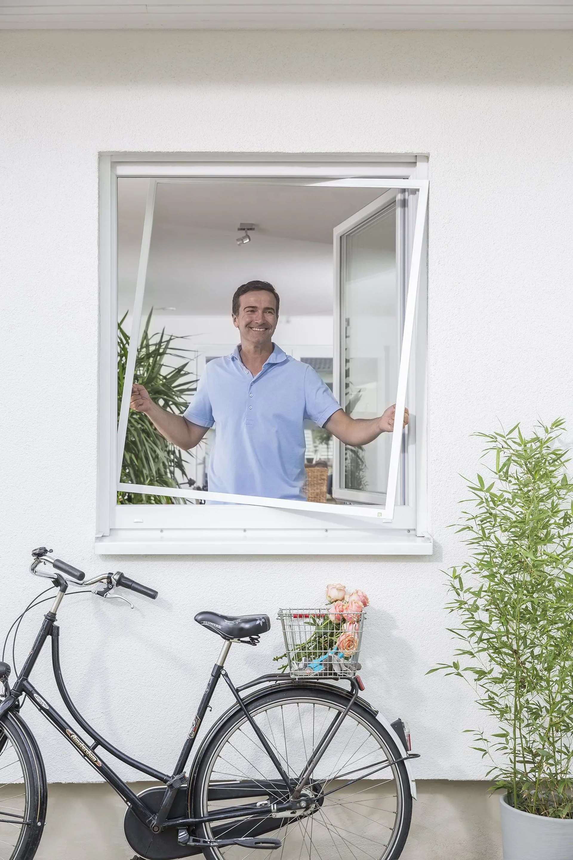 Mann öffnet ein Fenster mit Insektenschutz-Spannrahmen