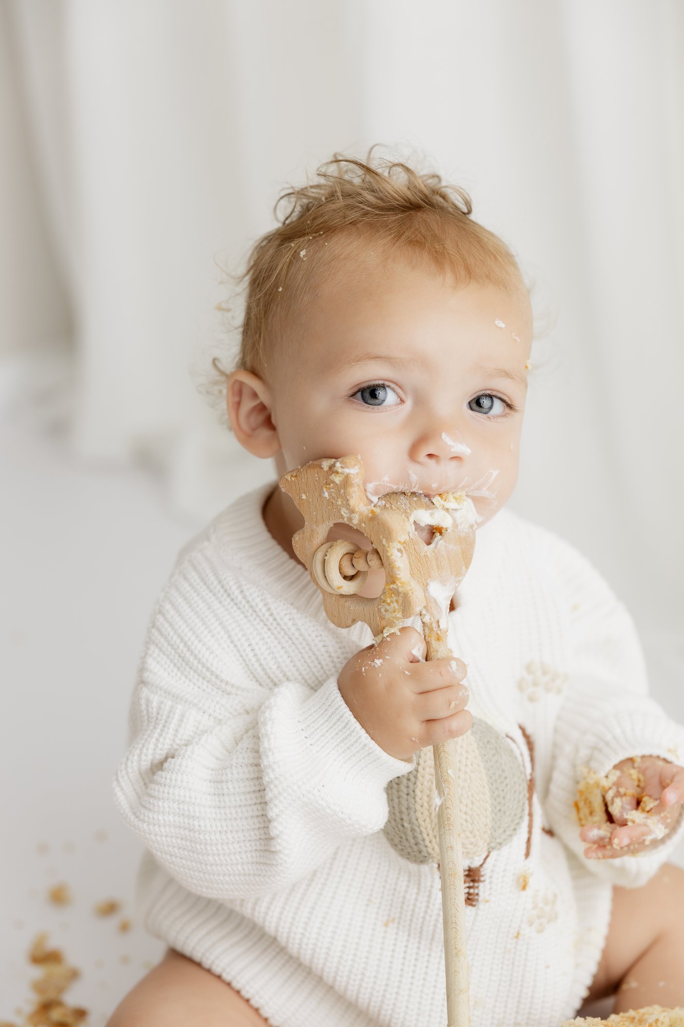 Kleinkind hält einen Holzlöffel mit Kuchen, Sahne im Gesicht