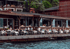 Outdoor restaurant on a wooden pier over water with many patrons dining at tables.