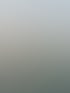 Eine lächelnde Frau in einer grünen Strickjacke und Brille steht vor einem ruhigen See bei Sonnenuntergang.