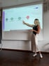 Eine blonde Frau steht vor einer Projektion mit der Aufschrift „Customized Podcast“ und zeigt auf ein Flussdiagramm.