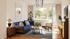 Modernes Wohnzimmer mit blauem Sofa, rundem Couchtisch, Holzmöbeln und großem Fenster mit Blick ins Grüne.