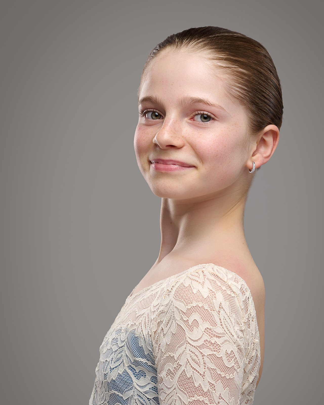 Audition-Porträtfoto: eine junge Tänzerin in einem blauen Trikot, die Haare zu einem Dutt zusammengebunden, vor einem schlichten grauen Studiohintergrund