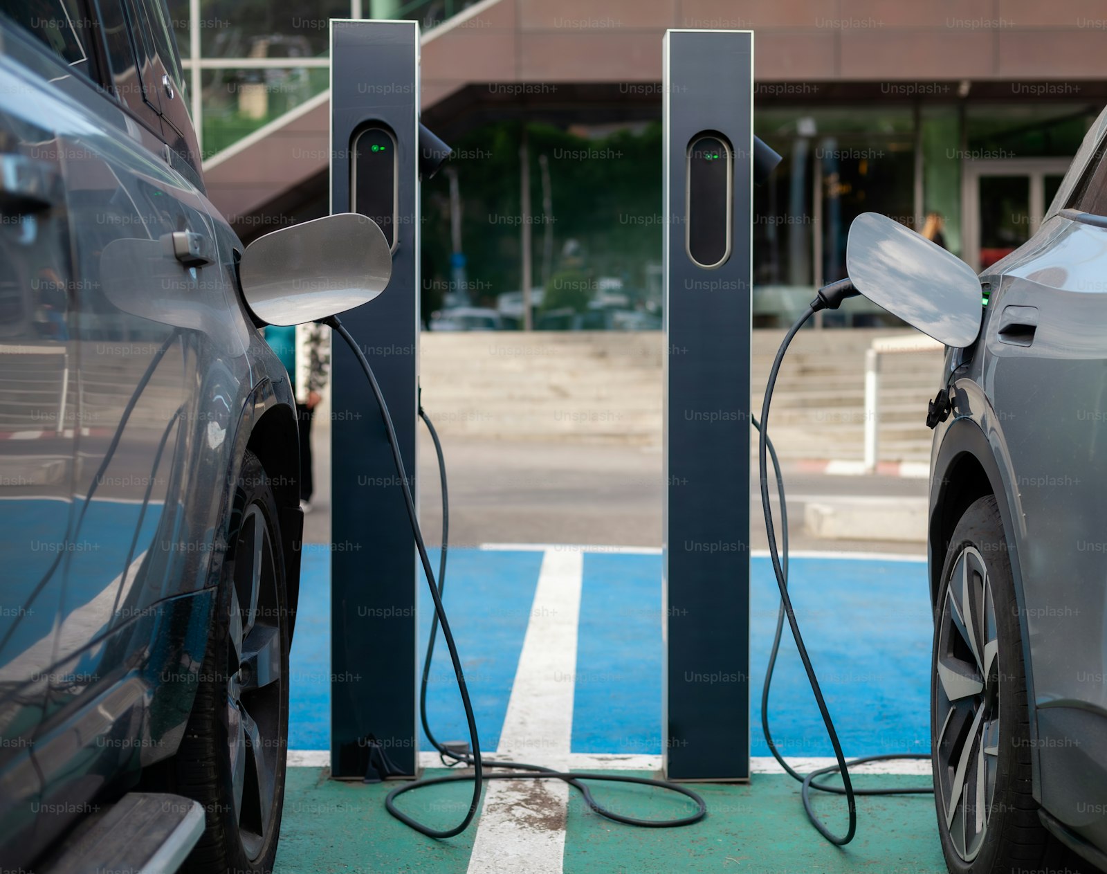 Two electric cars parked side by side and plugged in at a public charging station