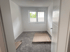 Leeres Zimmer mit grauem Teppichboden, weiß gestrichenen Wänden und einem Fenster mit Jalousien.