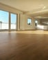 Ein sonnendurchflutetes, leeres Wohnzimmer mit hellem Eichenparkett, weißen Wänden und großen Fenstern zum Balkon.