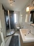 Modernes Badezimmer mit weiß gefliesten Wänden, Duschkabine, Toilette und Waschbecken mit Holzunterschrank.