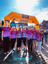 Sieben Menschen in pinken Diakonie-Laufshirts vor einem orangefarbenen Startbogen.