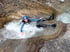 Eine Person in einem blauen Neoprenanzug und Helm treibt lächelnd auf dem Rücken in einem Fluss.