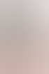 Eine beige Untersuchungsliege mit einem grauen Kissen und einem blauen Nackenkissen steht vor einer großen grünen Pflanze.