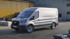 Silberner Ford Transit Kastenwagen parkt vor einem gelben Gebäude und grauen Säcken.