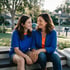 A smiling mother and daughter sit on porch steps in a suburban neighborhood wearing matching blue and orange shirts.