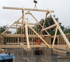 Ein Kran hebt einen großen Holzbalken auf ein teilweise fertiggestelltes Holzrahmenhaus eines Gewerbegebäudes.