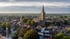 Luftaufnahme aus Erkelenz mit einer großen Kirche mit spitzem Turm inmitten von Wohnhäusern und Bäumen bei bewölktem Himmel.