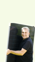Ein lächelnder Mann in schwarzem Poloshirt hält ein großes schwarzes Solarpanel.